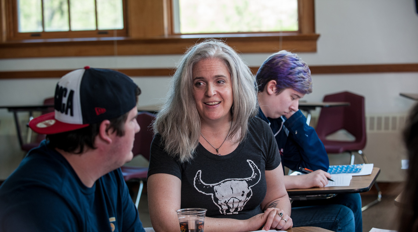 Shot of English Professor, Naomi Crummey, assisting a student while another student studies in the background.
