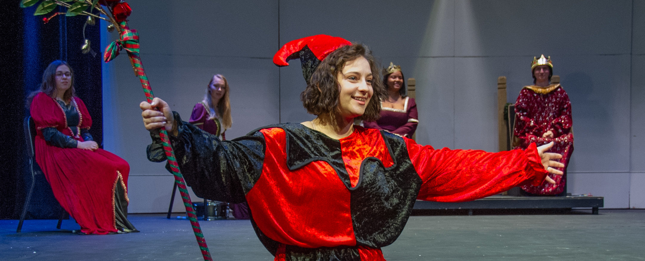 Blackburn student actor performing on stage at the Bothwell Auditorium. Four other student actors can be seen in the background. All of the actors are wearing medieval clothes. HELP