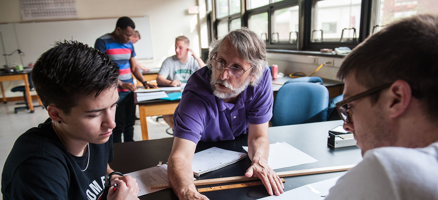 Blackburn professor assisting two students with their work.