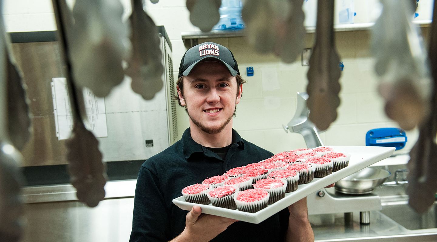 A Blackburn dining services student worker carries a tray of freshly baked cupcakes in the kitchen.