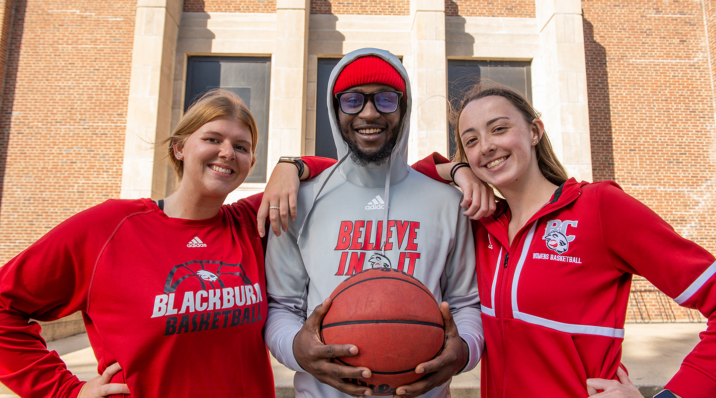 Three Blackburn College athletes posing in front of the entrance to the Dawes Gymnasium.