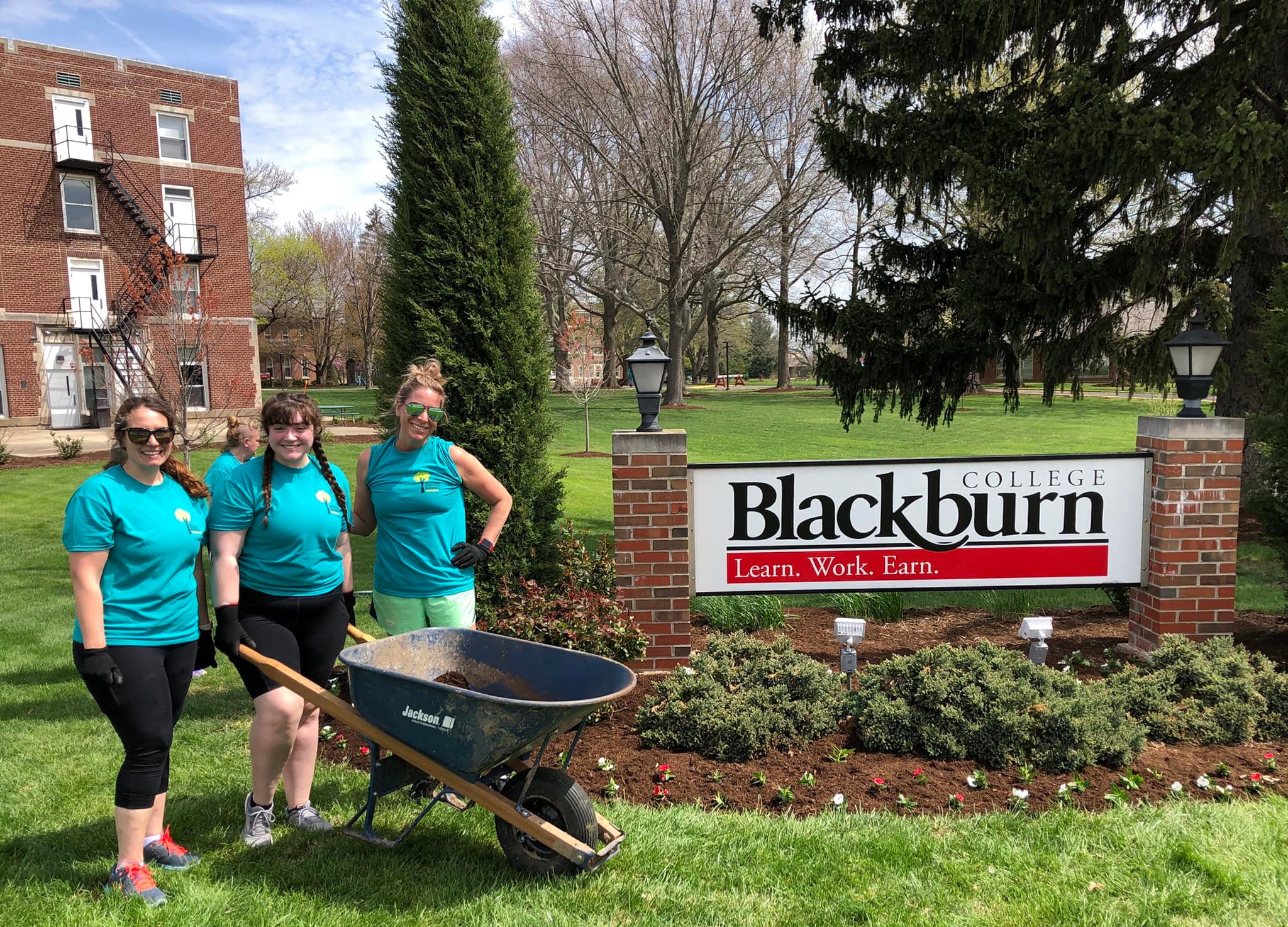 Three volunteers standing next to the Blackburn College sign on the 2022 Beautification Day. HELP