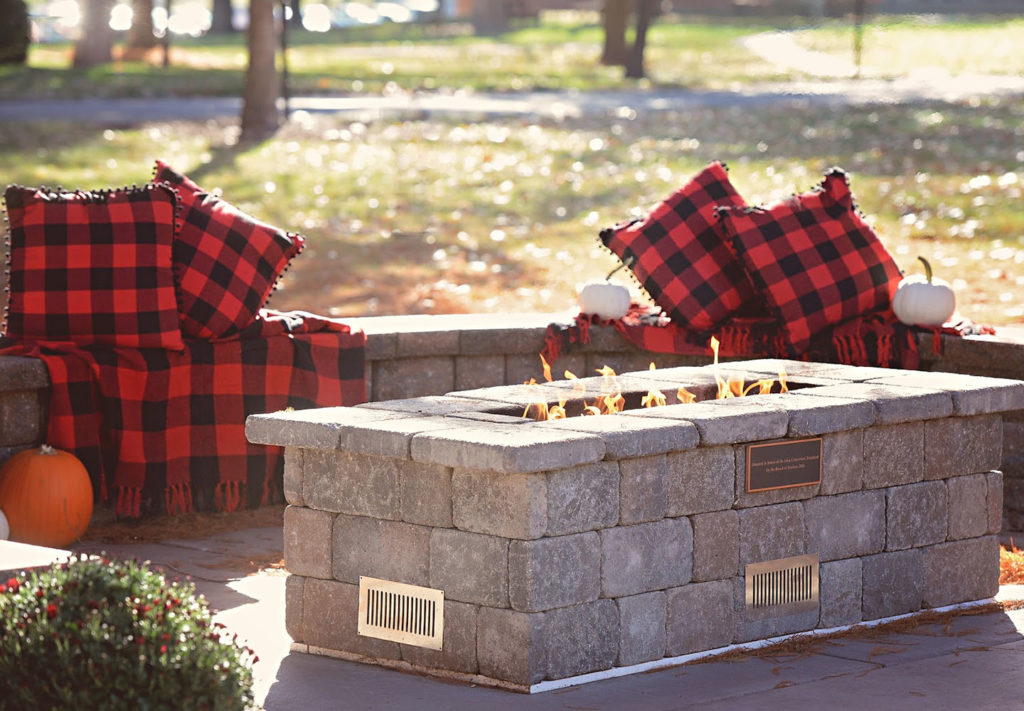 Wide shot of the firepit at Jaenke's patio. The area around the firepit is decorated with pillows and pumpkins.
