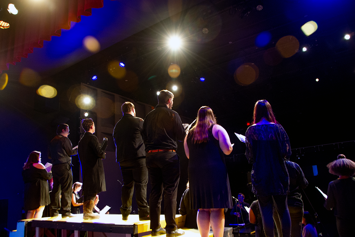 Blackburn College choir singing and standing on a platform, photographed on stage from the back of the stage facing towards the audience