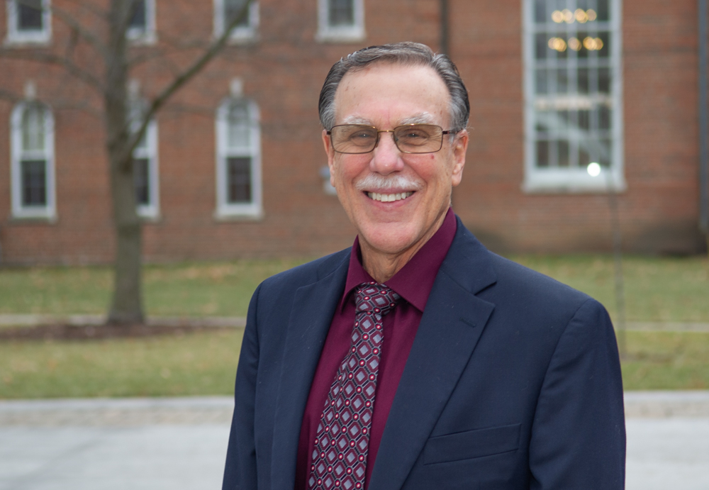 Blackburn College President Gregory J. Meyer, photographed outside Ludlum Hall - the main administration building. A brick facade with windows, built by Blackburn students as part of the nations only student-led Work Program