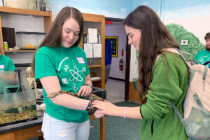 Blackburn student holding a snake while a high school student stands by and pets it. HELP