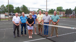 Seven individuals representing Blackburn College and community organization Winning Communities gather on the Blackburn College tennis courts and the future site of the "Winning Communities Pickleball Courts"