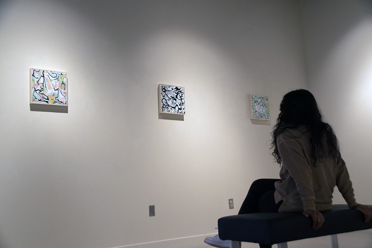 Woman sits in gallery on bench admiring three hanging abstract paintings
