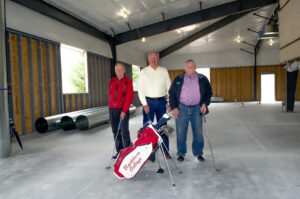 Three men stand together on construction site, future home of a golf performance center.