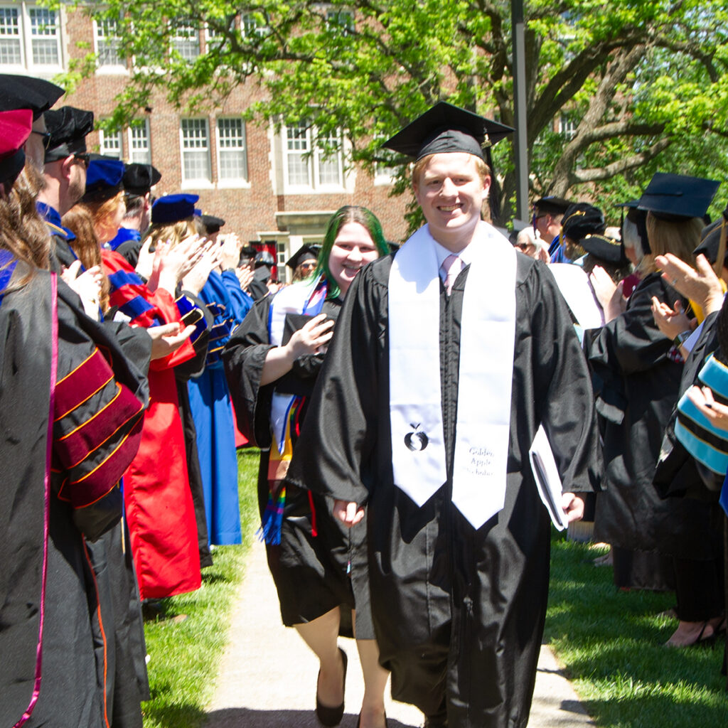 Class of 2024 Valedictorian Katilyn Nix and Salutatorian Evan Hopper walk down a sidewalk surrounded by Blackburn faculty during the Commencement Recession