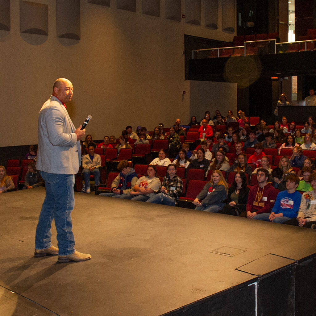 Students sit in Bothwell Auditorium with man on stage with microphone