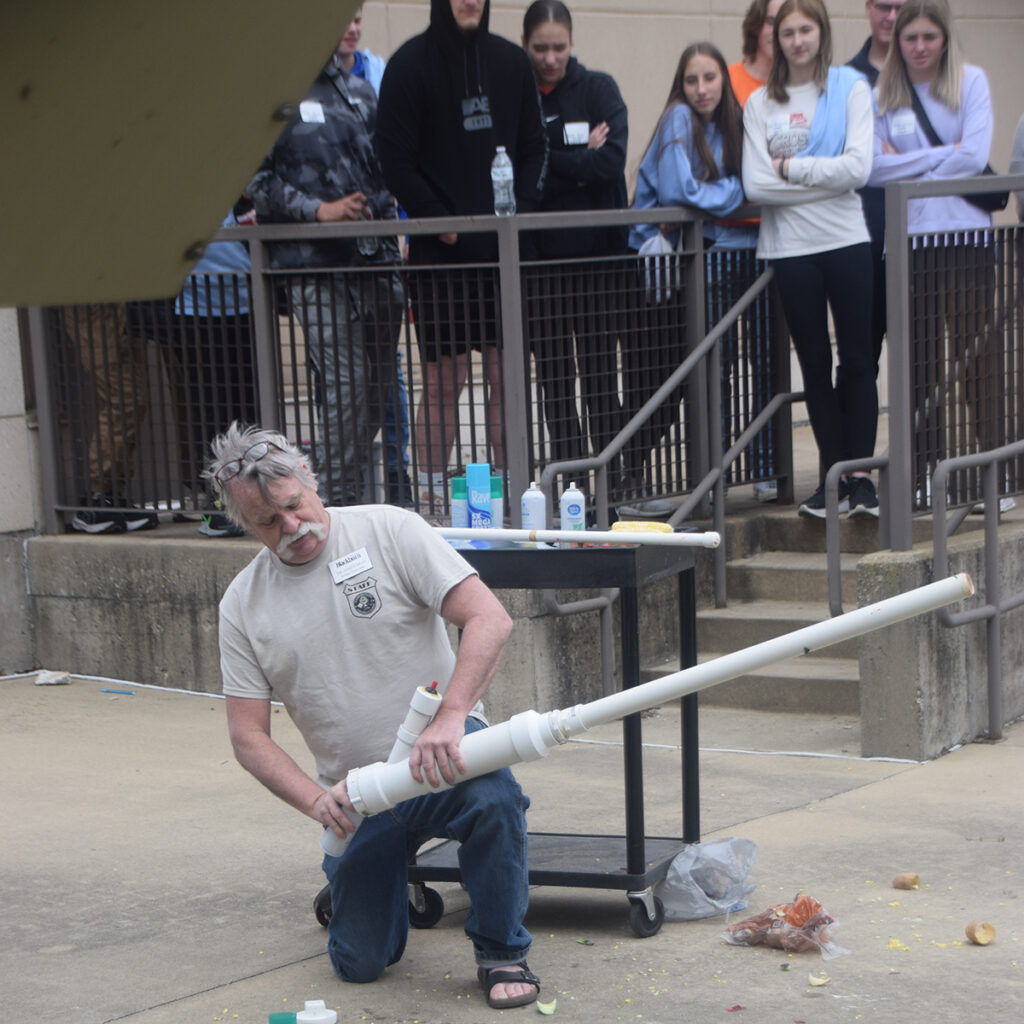 Students watch from a safe distance while professor demonstrates potato cannon.