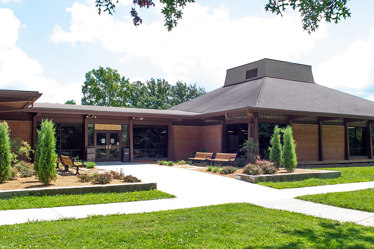 Exterior of Lumpkin Library - building with vaulted roof and nice landscaping, benches and trees line the side walk to the doors