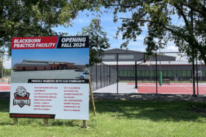 Construction Sign "Opening Fall 2024" with a rendering of Blackburn's new athletic center and a racquet and hoops complex in the background.