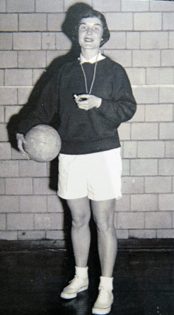 Marion Carlson, former professor and athletic director, stands holding a basketball and whistle in Dawes Gymnasium