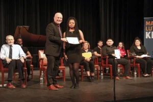 President stands with student, handing her a certificate on stage for winning the student leadership award during the MLK Convocation