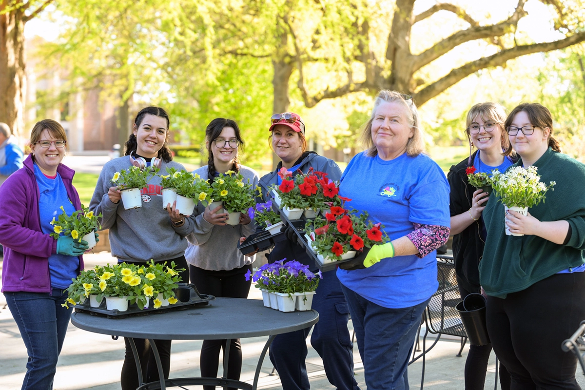 A group of people in event shirts stand with flowers to plant at Beautification Day at Blackburn