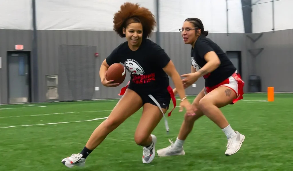Two women playing flag football inside indoor athletic facility