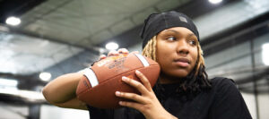 Woman with braids and head cover pulls arm and hand holding football back to throw