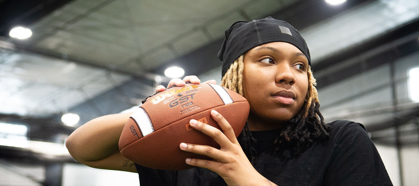Woman with braids and head cover pulls arm and hand holding football back to throw
