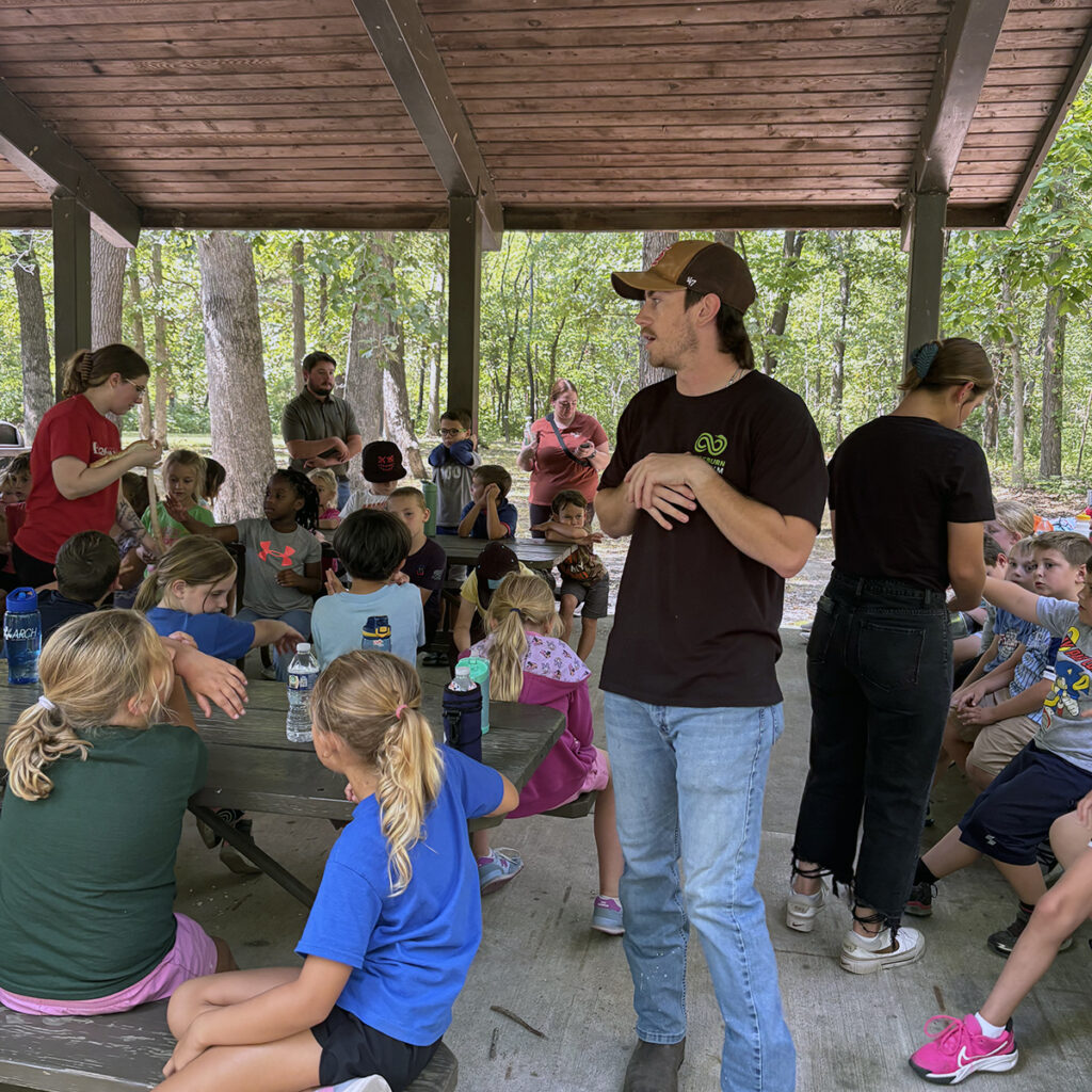 Several Blackburn students walk around speaking with second graders, while another Blackburn student stands in the middle of a pavilion sharing information