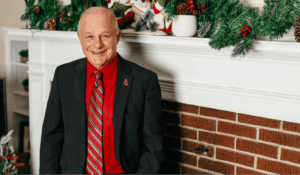 President Larry K. Lee stands in front of fireplace decorated for Christmas