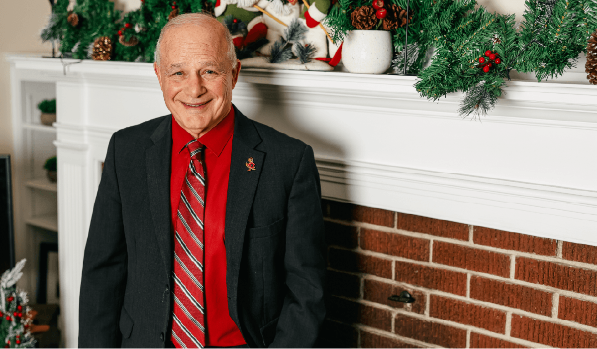 President Larry K. Lee stands in front of fireplace decorated for Christmas