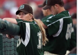 Justine Siegal, wearing a baseball uniform standing in a dugout leaning against the fence