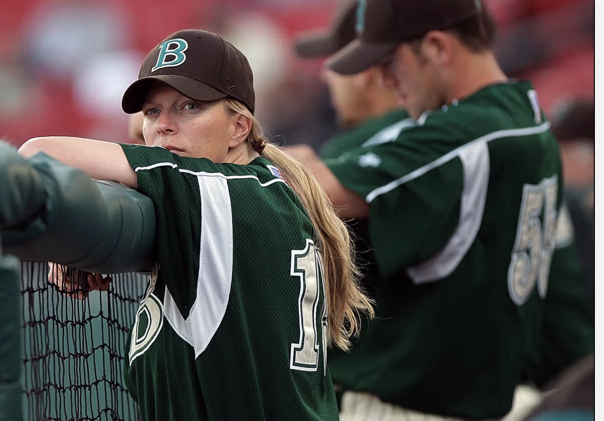 Justine Siegal, wearing a baseball uniform standing in a dugout leaning against the fence